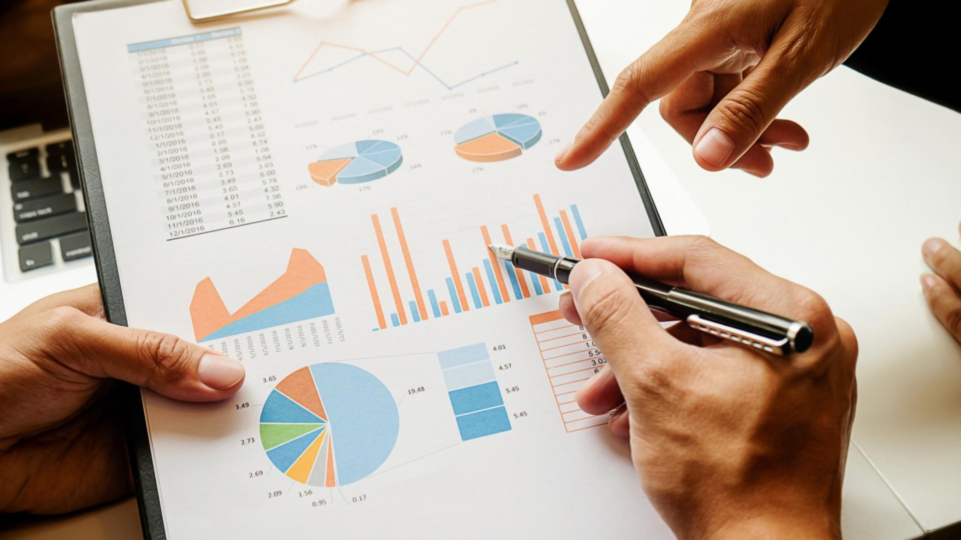  Close-up of hands analyzing a business report on a clipboard, featuring various charts and graphs